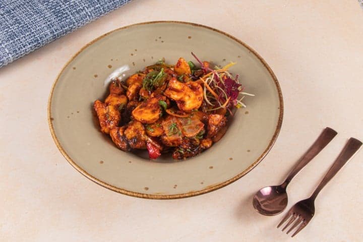 A vibrant dish of crispy chicken garnished with fresh greens is artfully presented on a rustic plate at Jugnoo Cafe in Gurugram, inviting travelers to savor the culinary delights in a cozy dining setting.