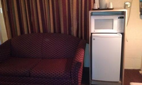 A cozy hotel room features a patterned sofa beside a compact fridge and microwave setup, creating a warm and functional space ideal for travelers seeking comfort and convenience.