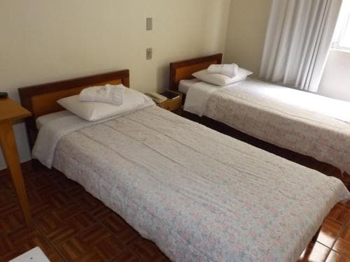 A cozy hotel room with two neatly made single beds adorned with floral bedding, wooden furnishings, and soft natural light filtering through sheer curtains, ideal for budget travelers seeking comfort.