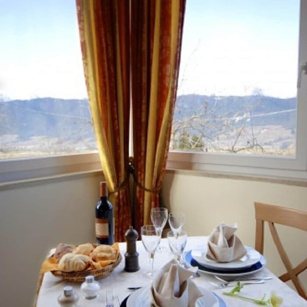 A cozy dining table set with bread, wine, and elegant glassware by a window with rich curtains, overlooking serene hills, ideal for a romantic getaway or a tranquil retreat.