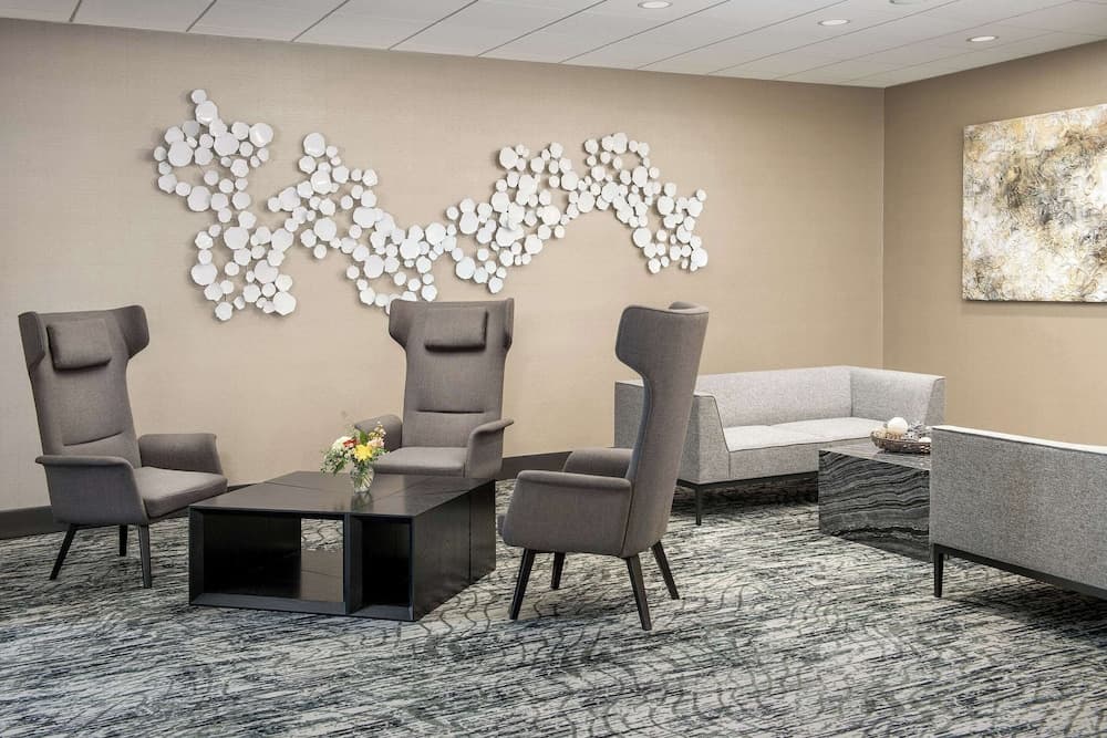 A modern waiting room features comfortable gray seating, abstract wall art, and a sleek coffee table, creating a calm and inviting atmosphere ideal for business travelers seeking a professional yet relaxing environment.