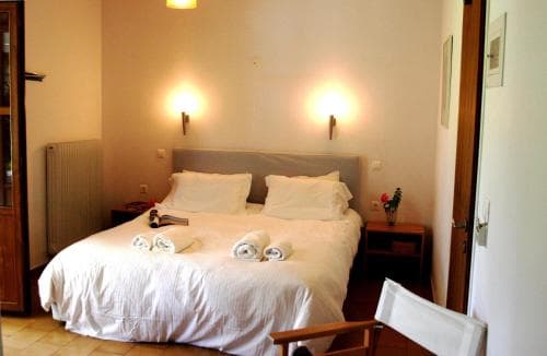 A cozy hotel room features a neatly made bed with white linens, warm wall sconces, and simple furnishings, creating an inviting atmosphere ideal for travelers seeking comfort and relaxation.