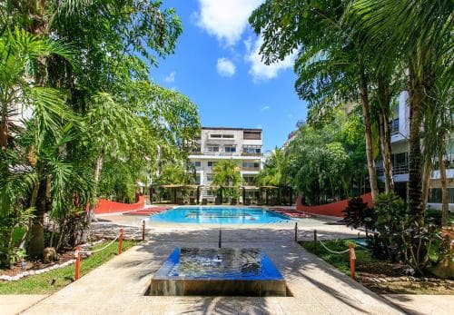 A serene tropical resort scene features a vibrant pool surrounded by lush palm trees under a sunny sky, ideal for vacationers seeking relaxation and leisure.