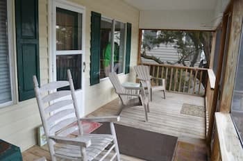 A cozy wooden porch with white rocking chairs and green shutters invites relaxation, perfect for travelers seeking a peaceful retreat in a quaint seaside setting.