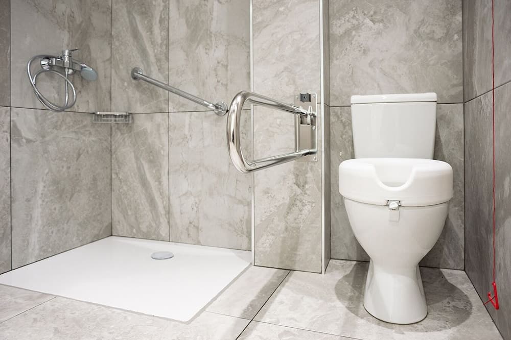 A modern accessible bathroom features a walk-in shower with a handheld showerhead, grab bars, and a raised toilet seat, ideal for travelers requiring mobility assistance.