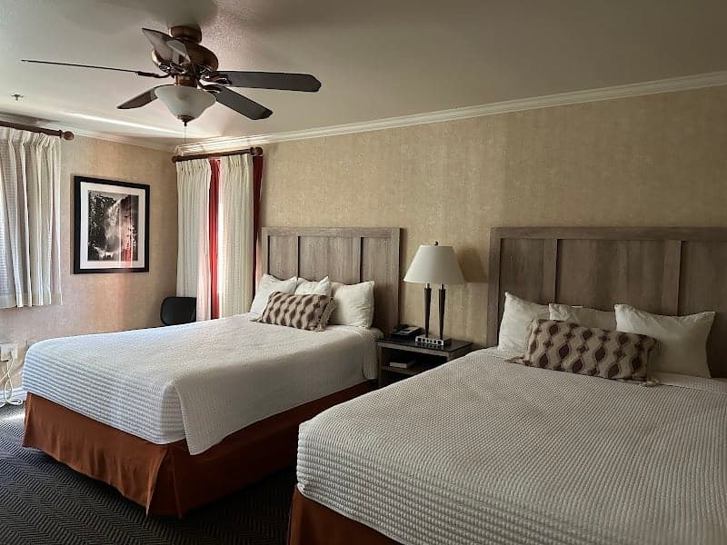 A cozy hotel room at Yosemite View Lodge features two neatly made beds, warm lighting, and a scenic view through the curtains, ideal for travelers seeking comfort near Yosemite National Park.