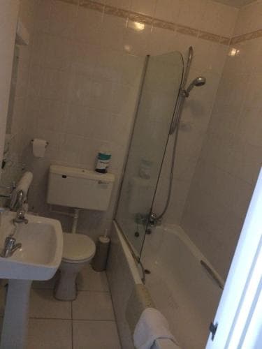 A compact bathroom with white tiled walls, a shower-over-bath setup, toilet, sink, and minimal decor offers a practical space for travelers seeking cleanliness and functionality in their accommodations.
