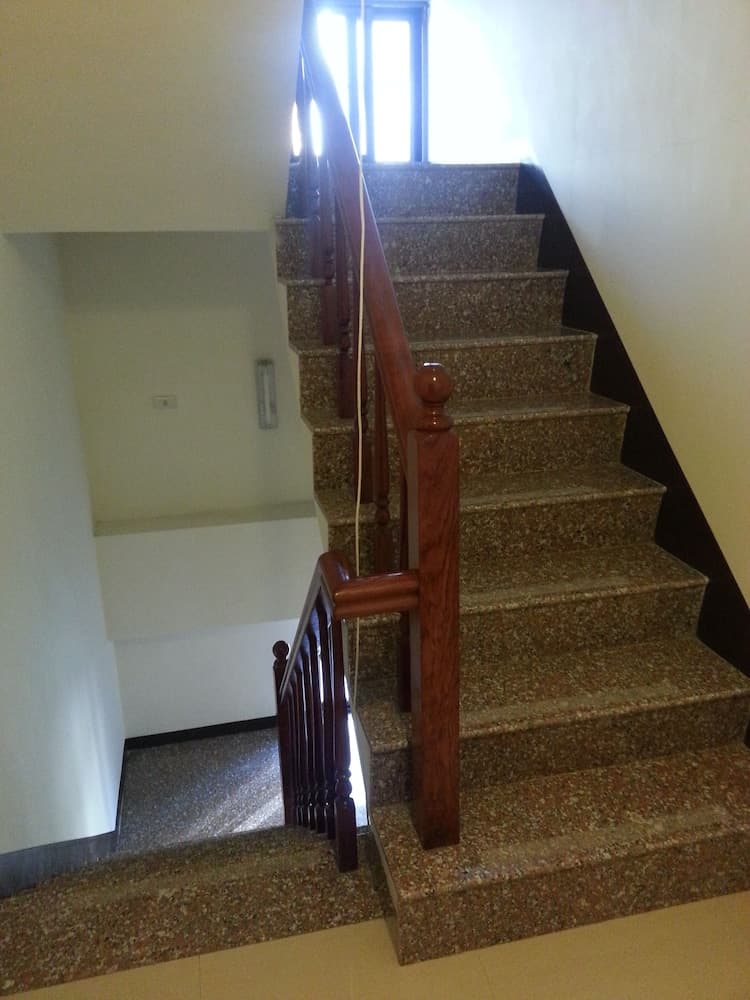A warmly lit indoor staircase with polished wooden railings and terrazzo steps leads to an upper level, ideal for exploring residential architecture and interior design trends.