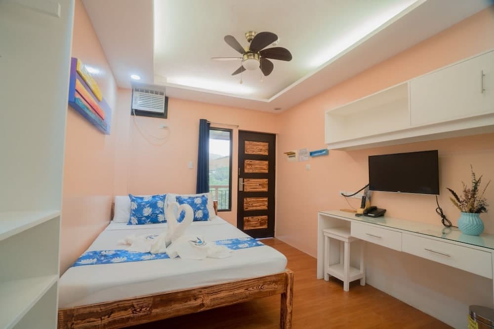 A cozy hotel room with peach walls, wooden furnishings, a neatly made bed adorned with blue accents, and a desk area featuring a TV, ideal for travelers seeking comfort and convenience in a serene setting.