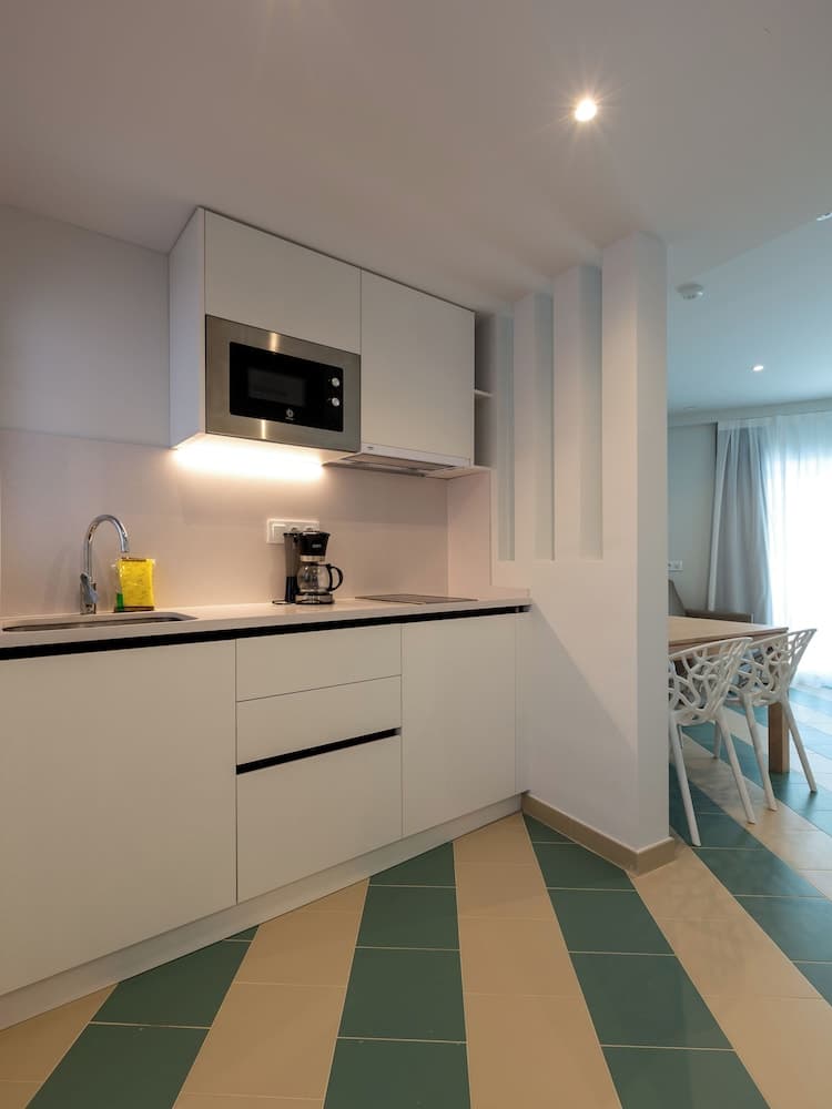 A modern kitchen with sleek white cabinets, a built-in microwave, and a striped green-and-white floor creates a clean and inviting atmosphere, ideal for travelers seeking a cozy self-catering accommodation.