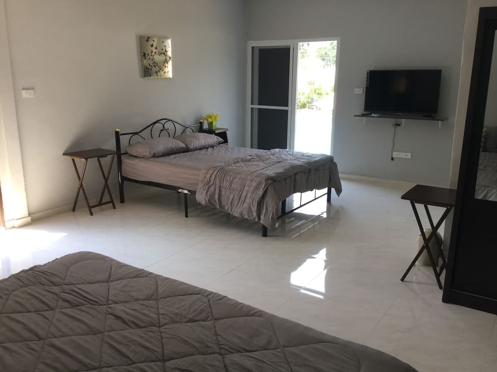A cozy bedroom with tiled floors, a neatly made bed, a wall-mounted TV, and a sliding glass door leading to greenery outside, ideal for travelers seeking a tranquil and modern accommodation.