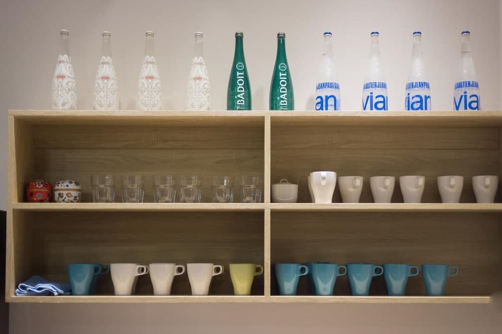 A neatly organized wooden shelf displays an array of colorful cups, glasses, and bottles in a modern kitchen setting, ideal for showcasing home decor or interior design inspiration.