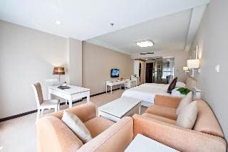 A cozy hotel suite features a modern living area with beige sofas, a dining table, and a flat-screen TV, creating a welcoming atmosphere ideal for travelers seeking comfort and relaxation.