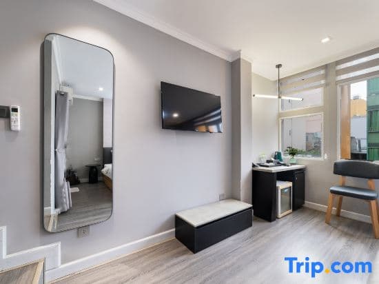 A cozy modern studio apartment features sleek furnishings, a mounted TV, and large windows letting in natural light, ideal for travelers seeking comfort and convenience.