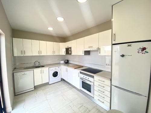 A bright, modern kitchen with white cabinetry, stainless steel appliances, and tiled flooring creates a clean and inviting atmosphere, ideal for travelers seeking a cozy self-catering accommodation.