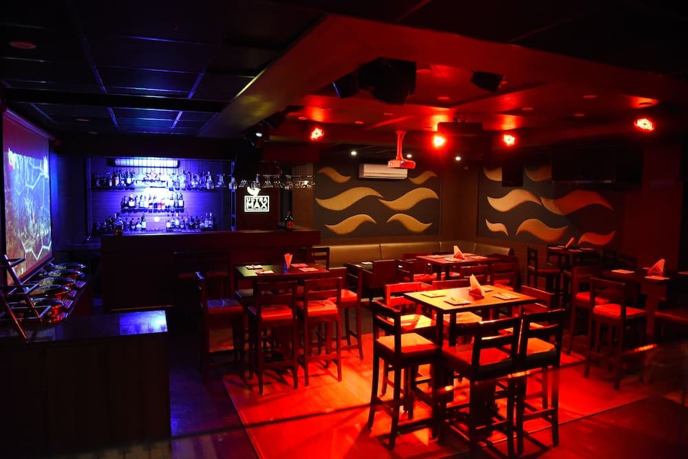 A cozy bar with vibrant red lighting, wooden tables, and a well-stocked bar area creates an inviting atmosphere perfect for evening social gatherings.