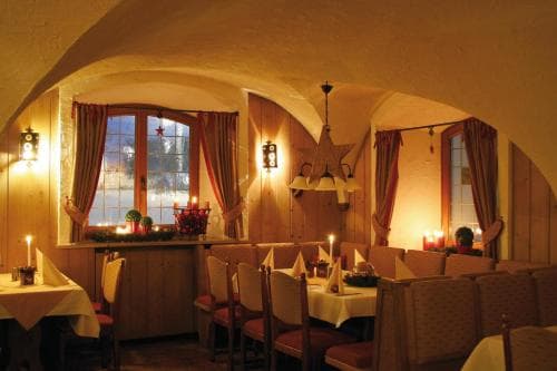 A cozy restaurant interior with arched ceilings, candlelit tables, and festive window decorations creates a warm and inviting atmosphere perfect for intimate dining experiences.