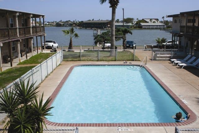 A serene waterfront resort features a sparkling pool surrounded by palm trees, lounge chairs, and nearby accommodations, ideal for a relaxing vacation getaway.