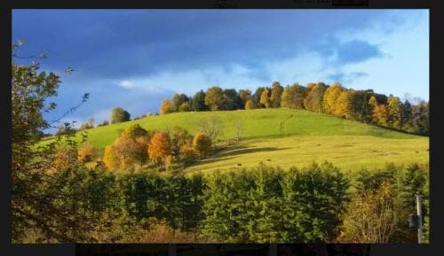 A serene rural landscape features rolling hills dotted with autumn-colored trees under a dramatic sky, ideal for nature photography and tranquil getaways.