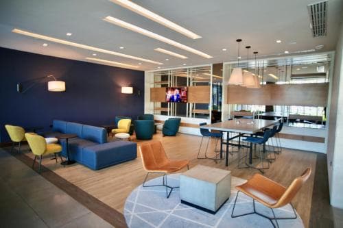 A modern, cozy lounge area with vibrant blue seating, stylish chairs, and a sleek dining space creates an inviting atmosphere ideal for travelers seeking relaxation or business meetings in a hotel common area.