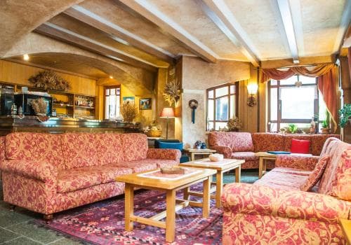 A cozy hotel lounge features plush patterned sofas, wooden tables, and rustic decor under a vaulted ceiling, creating an inviting atmosphere perfect for travelers seeking relaxation.