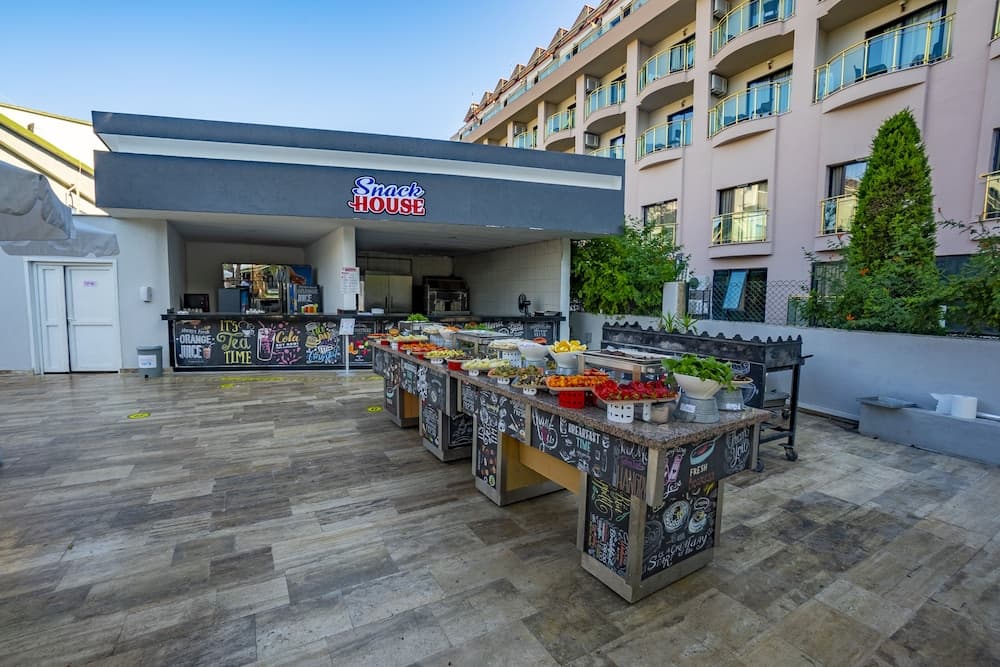 A vibrant outdoor snack bar with colorful displays of fresh fruits and beverages invites travelers to enjoy a casual dining experience in a sunny urban courtyard setting.