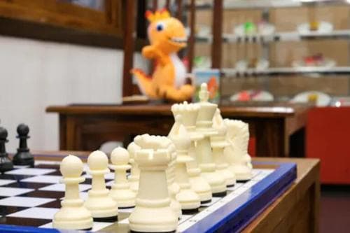 A cozy indoor setting features a chessboard with white pieces in focus, surrounded by playful decor including a plush dragon toy, ideal for travelers seeking unique cultural or family-friendly experiences.
