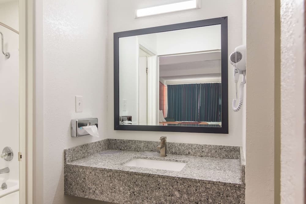 A clean hotel bathroom features a granite countertop sink, a large mirror, a mounted hairdryer, and a tissue dispenser, ideal for travelers seeking comfort and convenience.