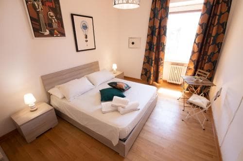 A cozy hotel room with a neatly made bed, warm wooden floors, patterned curtains, and framed artwork creates an inviting atmosphere perfect for travelers seeking comfort and relaxation.