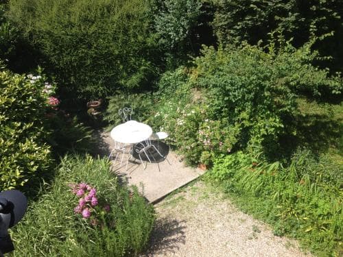 A serene garden patio surrounded by lush greenery and blooming flowers offers a tranquil spot for relaxation, ideal for travelers seeking peaceful outdoor retreats.