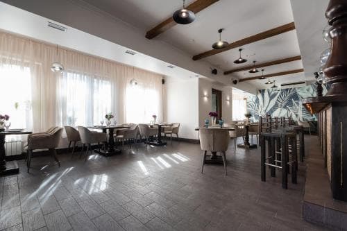 A cozy restaurant interior with wooden beams, tiled floors, and large windows casting natural light, featuring tables set for dining and a decorative mural, ideal for travelers seeking a relaxed dining experience.