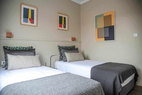A cozy hotel room features two neatly made beds adorned with modern art on the walls, creating a serene and stylish atmosphere ideal for travelers seeking comfort and simplicity.