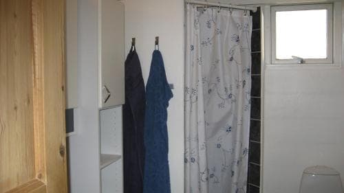 A cozy bathroom with a floral shower curtain, hanging towels, and natural light from a small window, ideal for travelers seeking a simple and functional accommodation space.