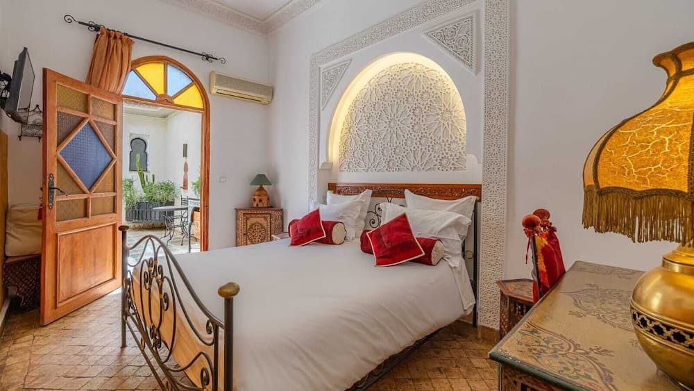 A cozy, ornately decorated bedroom with intricate wall carvings, vibrant red cushions, and a golden lamp exudes a warm, inviting atmosphere perfect for a luxurious retreat in a boutique hotel.