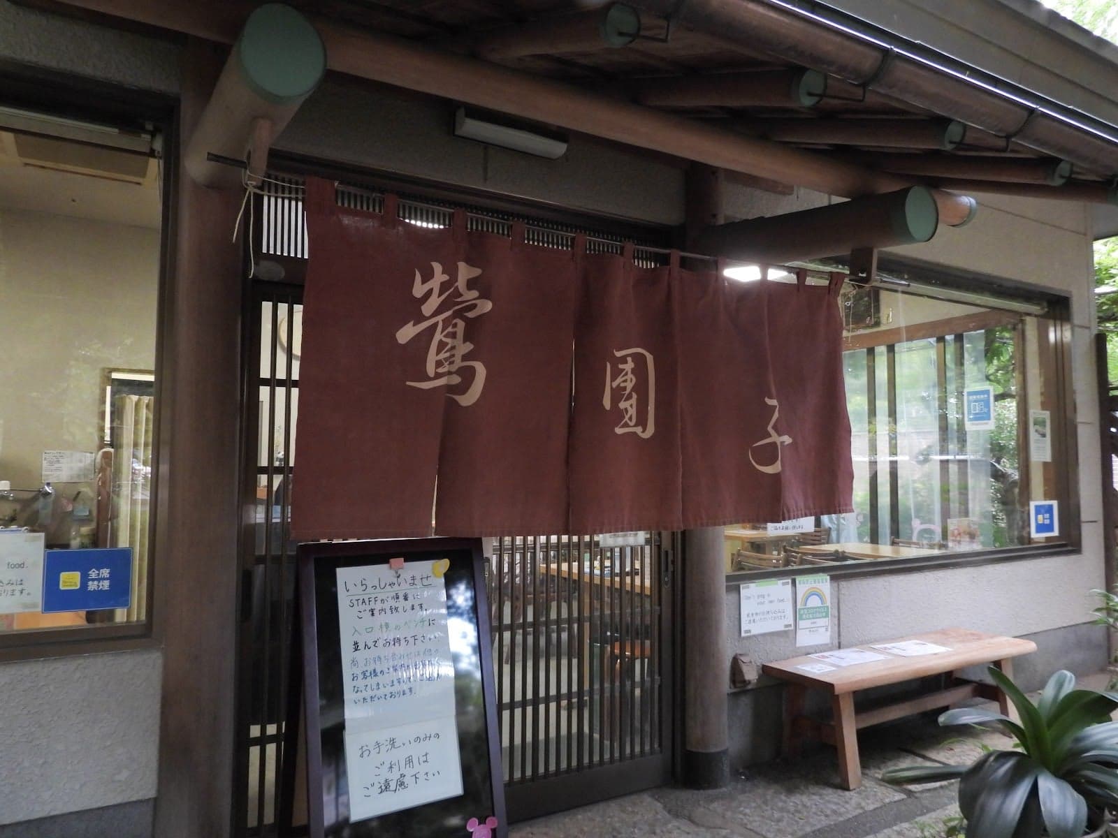 A serene Japanese tea house entrance in Ueno Park, Tokyo, features traditional wooden architecture, a welcoming noren curtain, and a cozy outdoor bench, ideal for travelers seeking cultural immersion and relaxation.
