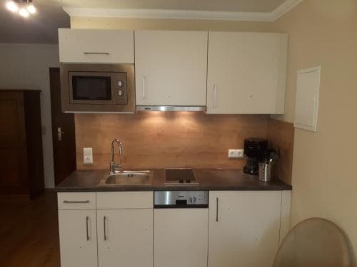 A cozy apartment kitchen featuring white cabinets, a stainless steel sink, and a microwave, exudes a modern and functional vibe ideal for travelers seeking self-catering accommodations.