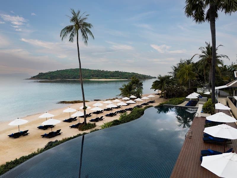 A serene tropical resort scene features an infinity pool overlooking a sandy beach lined with lounge chairs and umbrellas, surrounded by lush palm trees, ideal for luxury relaxation and vacation photography.