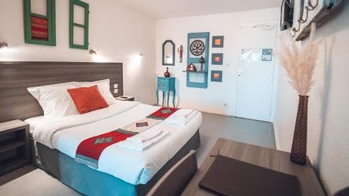 A cozy hotel room features a neatly made bed with vibrant bedding, colorful wall art, and decorative elements, creating a welcoming atmosphere ideal for travelers seeking comfort and style.
