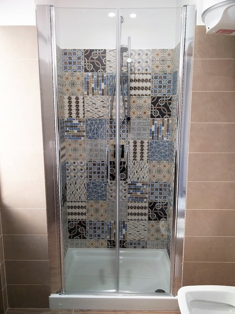 A modern bathroom features a stylish walk-in shower with intricate mosaic tiles, framed by sleek glass doors, ideal for travelers seeking contemporary design inspiration.