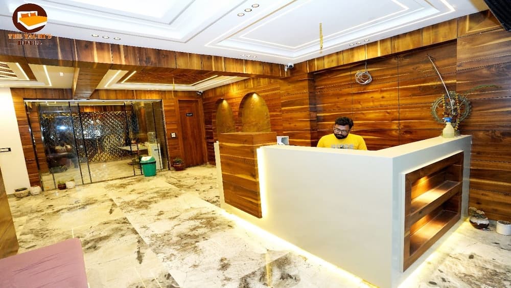 A warmly lit hotel lobby with wooden paneling, marble flooring, and a reception desk creates an inviting atmosphere, ideal for travelers seeking comfort and modern amenities.