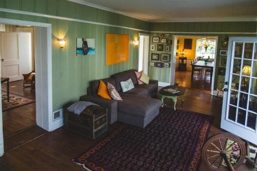 A cozy living room with green walls, vibrant artwork, and eclectic furniture creates a warm and inviting atmosphere, perfect for travelers seeking a comfortable and artistic retreat.