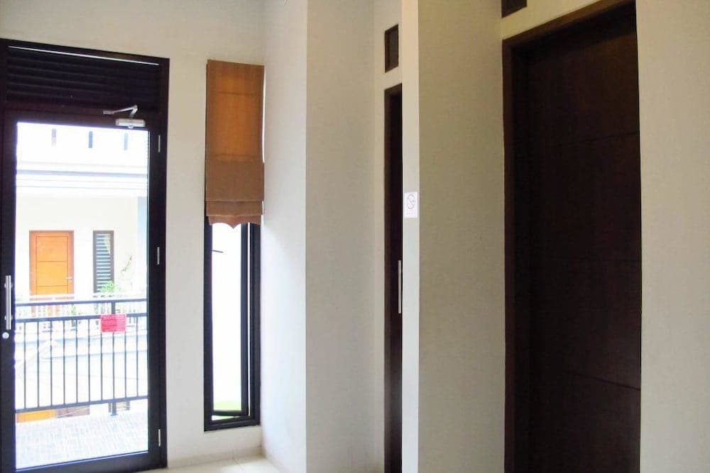 A serene indoor hallway with white walls, wooden accents, and a glass door leading to a balcony offers a tranquil atmosphere ideal for travelers seeking a peaceful accommodation experience.