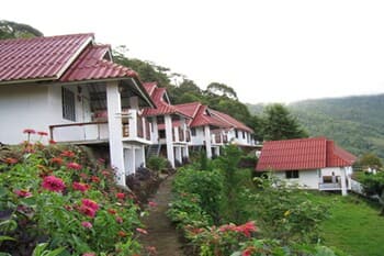 A serene tropical resort with white houses featuring red roofs nestled among lush greenery and vibrant flowers, ideal for a tranquil getaway in a mountainous region.