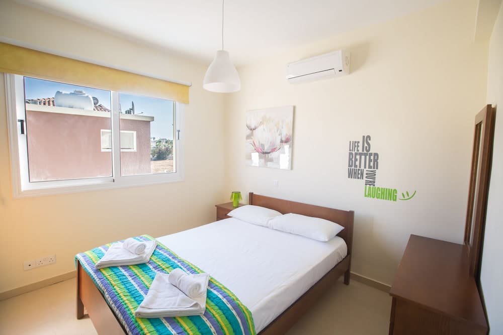 A cozy hotel room with a neatly made bed, vibrant striped blanket, motivational wall art, and a window view of rooftops, ideal for travelers seeking comfort and relaxation.
