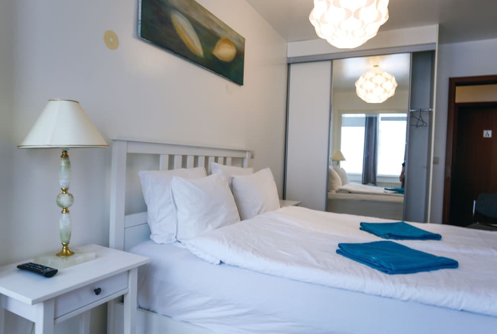 A cozy hotel room features a neatly made bed with white linens, blue towels, a stylish bedside lamp, and a mirrored wardrobe, creating a serene and inviting atmosphere ideal for travelers seeking comfort and relaxation.