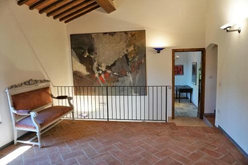 A cozy indoor space with terracotta flooring, a vintage armchair, and a large abstract painting creates an inviting atmosphere in a rustic villa, perfect for travelers seeking a charming retreat.