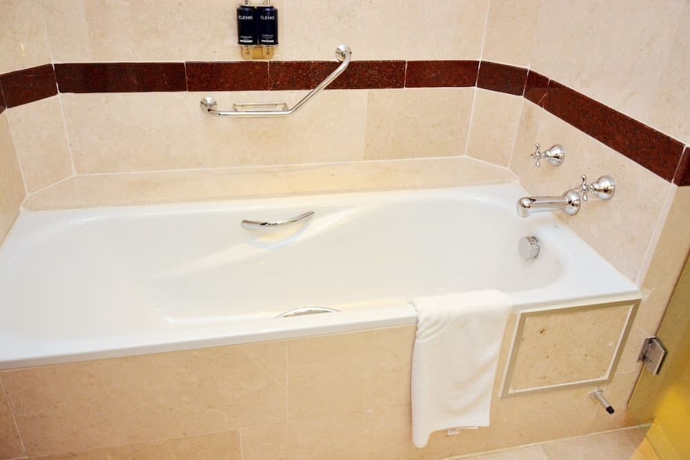 A luxurious hotel bathroom features a pristine white bathtub with elegant chrome fixtures, tiled walls in beige and brown tones, and neatly placed toiletries, ideal for travelers seeking comfort and relaxation.
