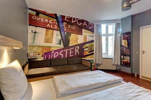 A cozy hotel room features a vibrant mural wall, wooden floors, and large windows, creating an artistic and inviting atmosphere ideal for travelers seeking a unique stay.