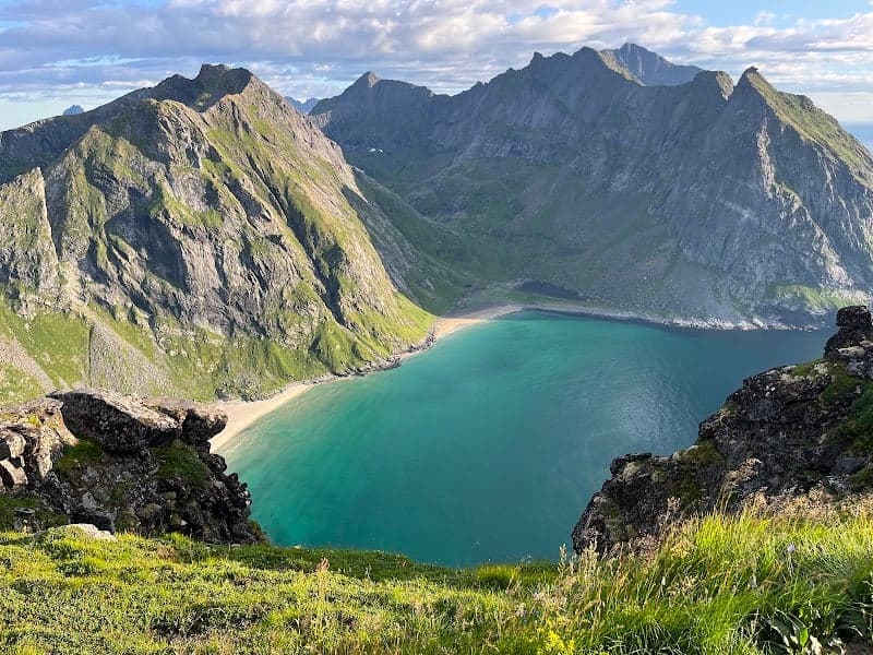 A breathtaking view of a secluded beach nestled between towering mountains, with turquoise waters and lush greenery, ideal for hikers exploring the scenic trails of Norway's natural beauty.