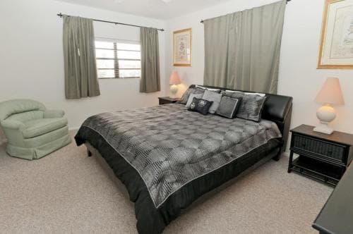 A cozy bedroom with a neatly made bed, soft green armchair, and framed artwork exudes comfort and relaxation, ideal for travelers seeking a peaceful retreat.